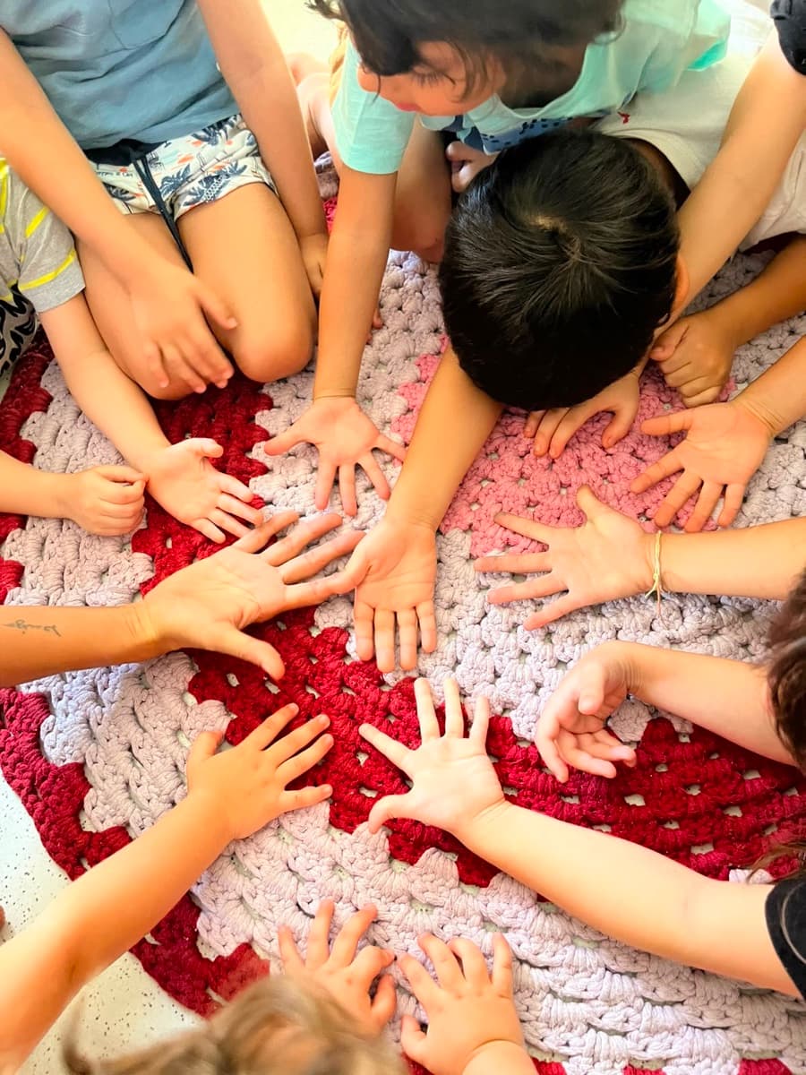 Roda de crianças apoiando as mãos sobre tapete